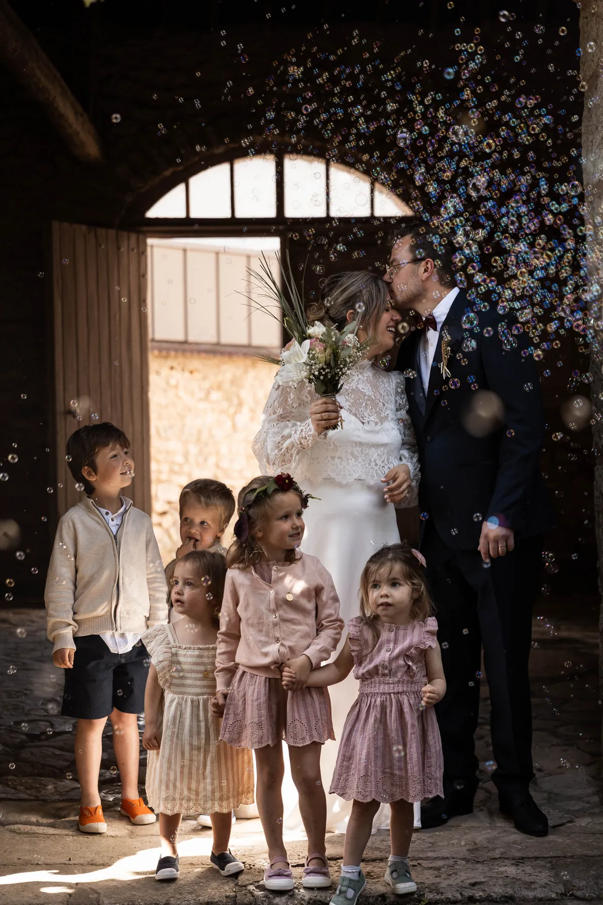 Baiser des mariés sous une pluie de bulles, entourés des enfants d’honneur