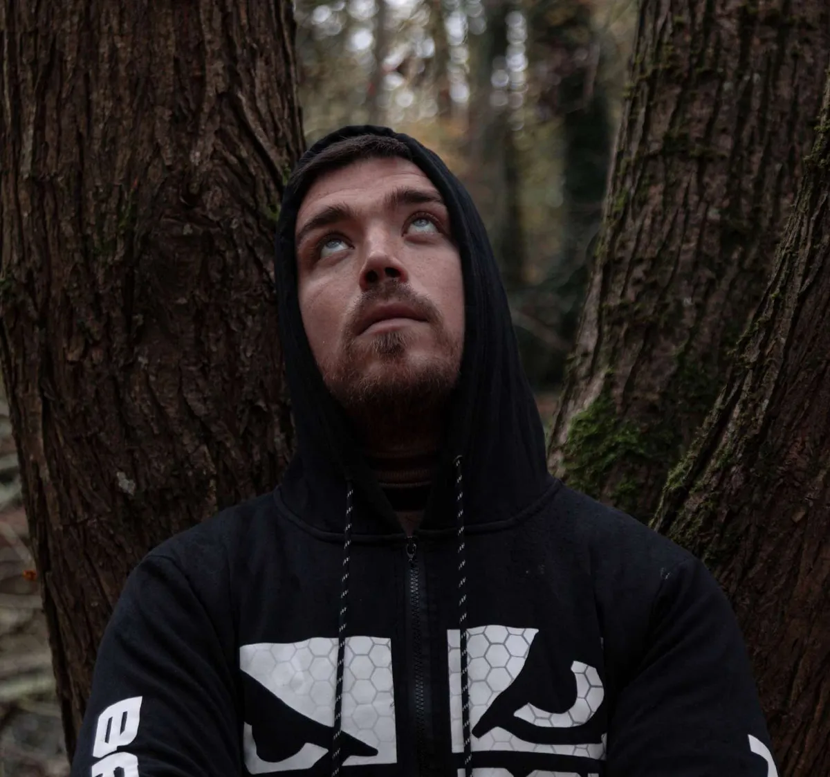 Portrait d’un homme en sweat à capuche adossé à un arbre